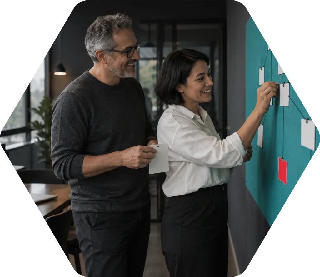 Duas pessoas organizando etapas em um quadro de post-its